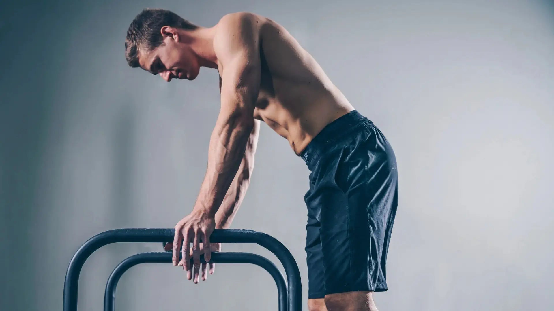 Man in athletic wear standing next to a barbell on a plain background